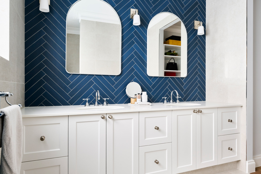 Custom home bathroom on Lombardy Street featuring blue herringbone tiles, white cabinetry, brass tapware and an arched mirror.