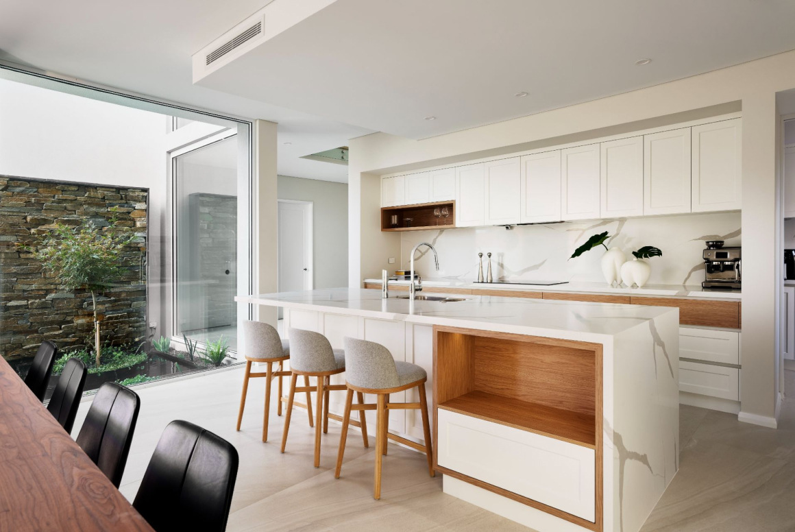 Custom home kitchen at The Grove in Wembley featuring white cabinetry, stone benchtops and timber bar stools.