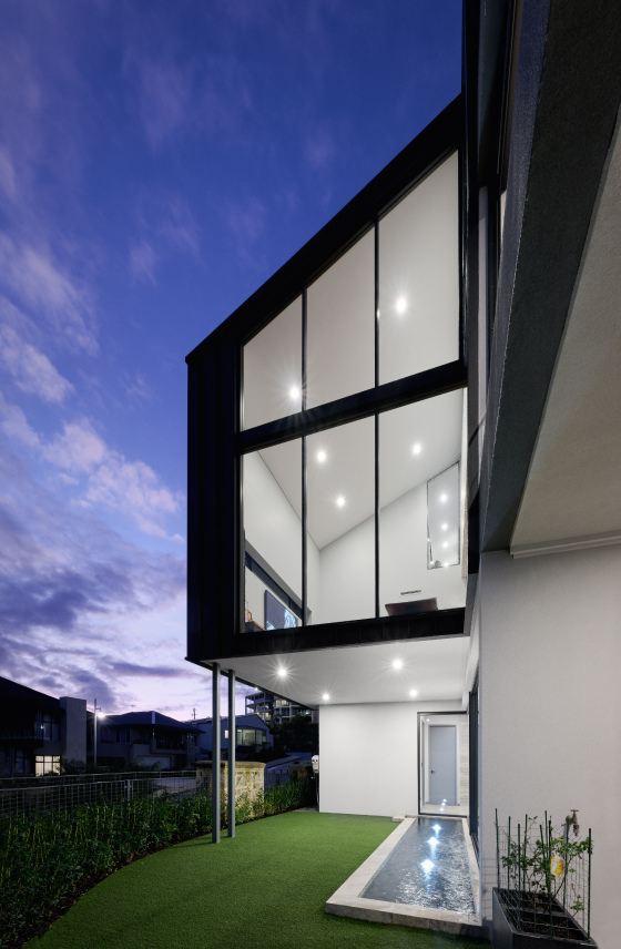 Three-storey custom home featuring full-height glazing, dark exterior cladding and illuminated interiors.
