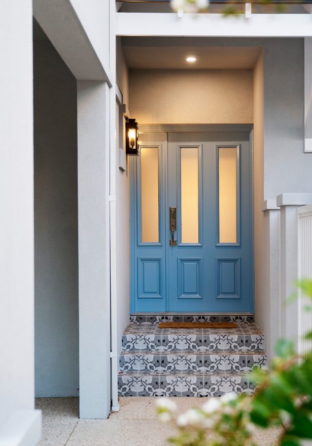 Covered entry walkway featuring timber decking, architectural lighting and a blue entry door.