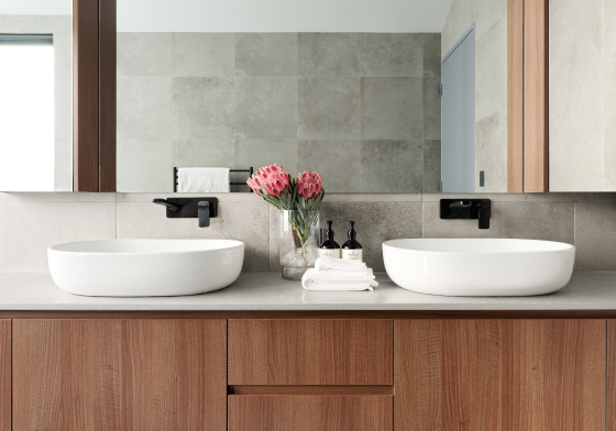 Custom home bathroom featuring a double vanity, stone benchtop, wall-mounted tapware and decorative flowers.
