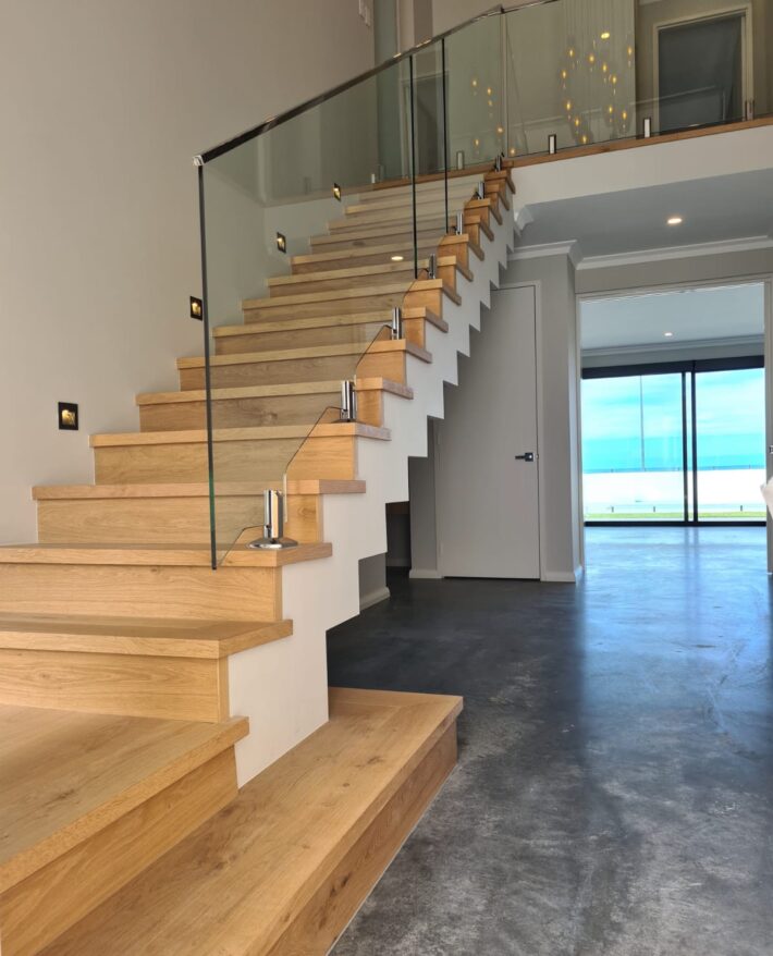 Floating timber staircase with glass balustrading, burnished concrete flooring and large windows in an Ocean Reef custom home.