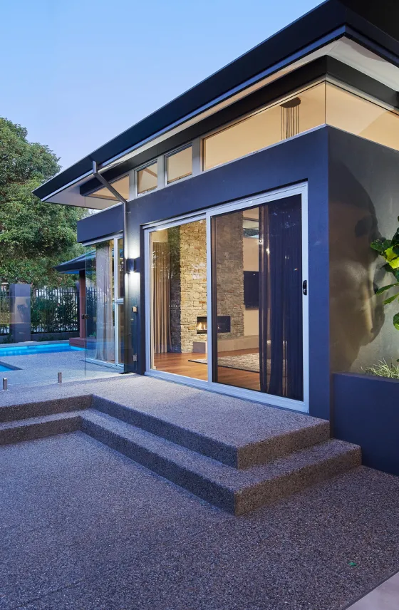 Rear entrance of a custom home featuring large glass doors, landscaped gardens and direct access to the poolside area.