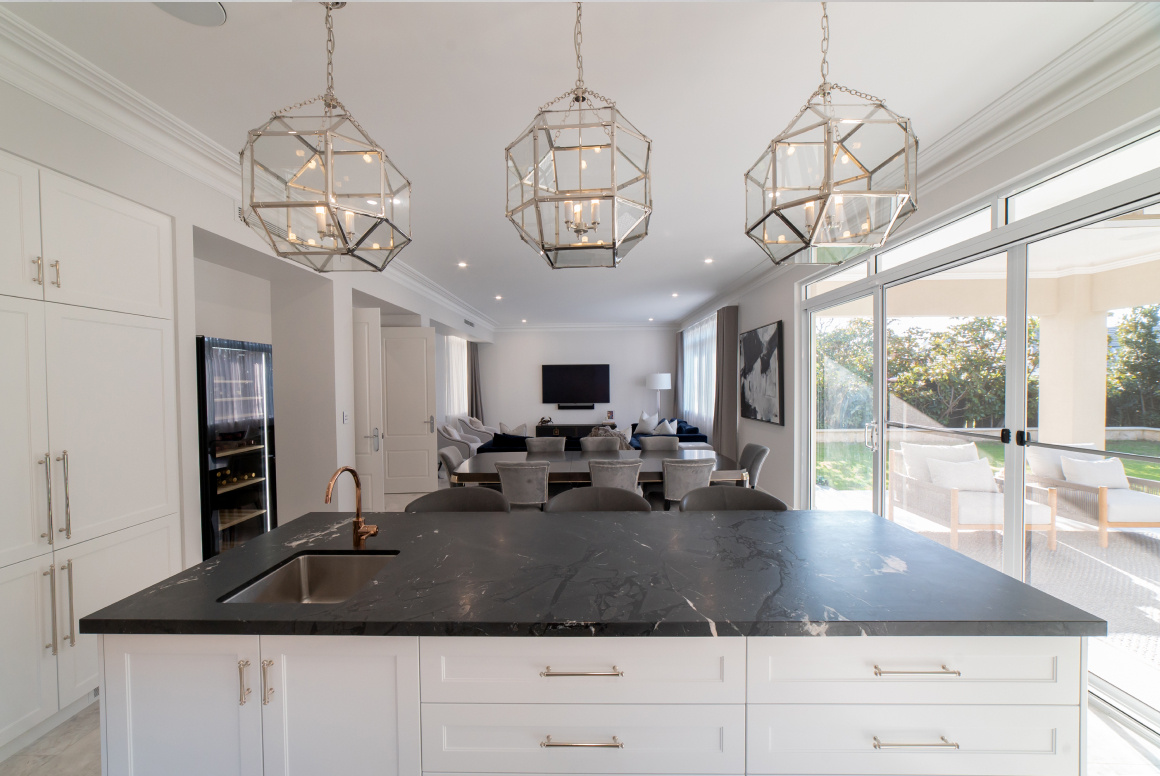Open-plan kitchen featuring a large island bench, decorative pendant lights and expansive glazing.