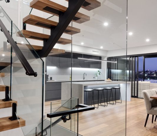 Three-storey custom home interior featuring a floating timber staircase, glass balustrading and expansive glazing.