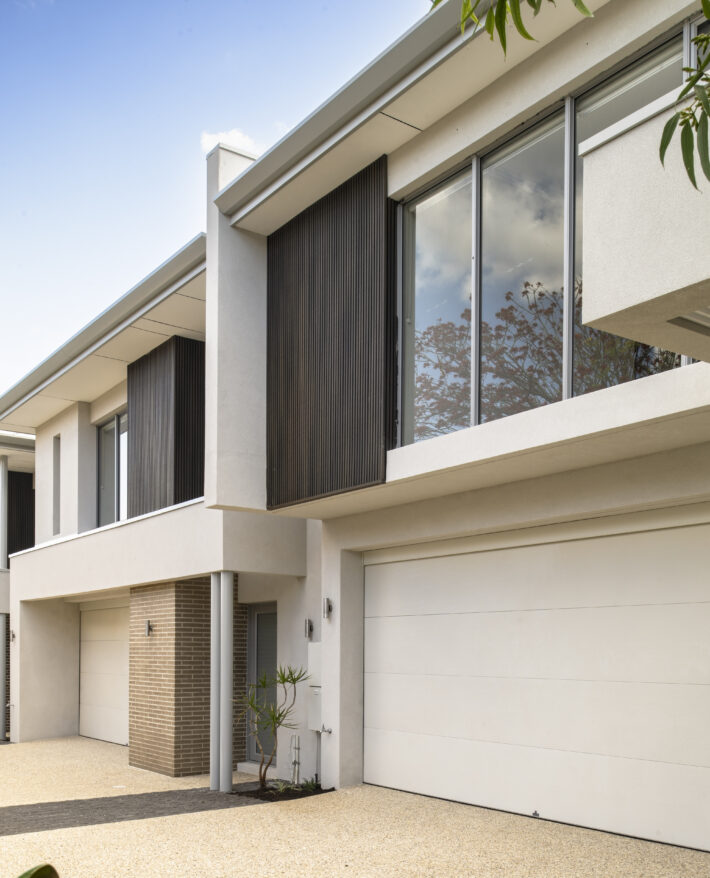 Contemporary two-storey custom homeS featuring light-coloured exterior materials, large windows and paved outdoor areas.