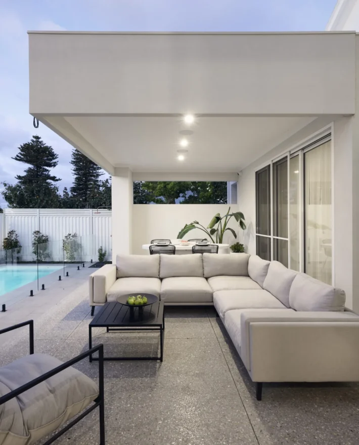 Covered outdoor living area at a Wembley custom home featuring contemporary seating, timber ceiling detailing and garden views.