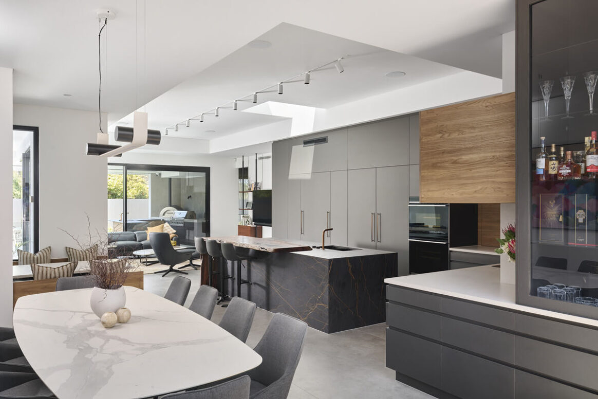 Modern kitchen featuring dark cabinetry, stone benchtops and open-plan living in a custom-designed Perth home.