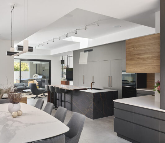 Modern kitchen featuring dark cabinetry, stone benchtops and open-plan living in a custom-designed Perth home.