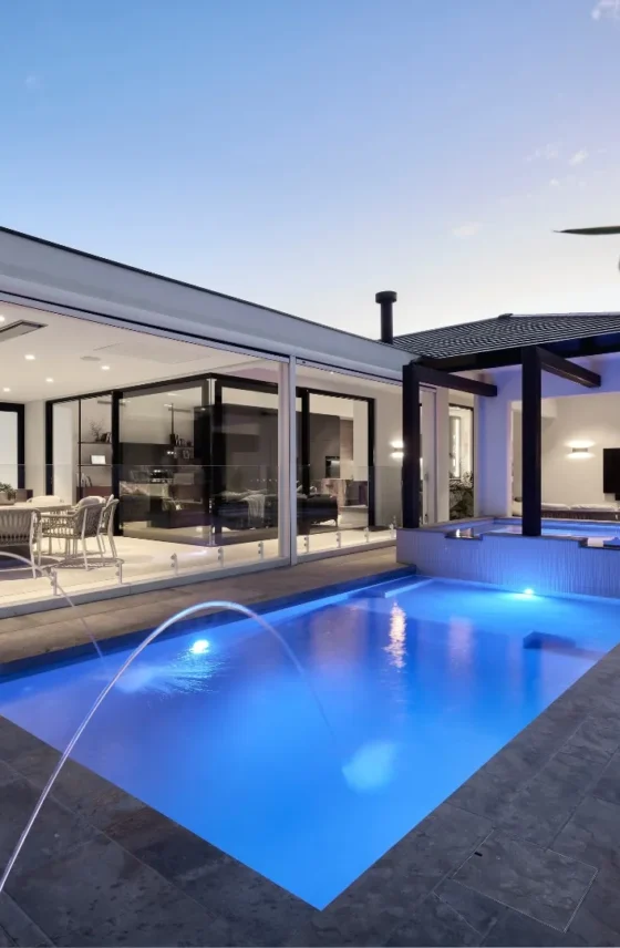 Custom home outdoor entertaining area featuring a swimming pool, covered alfresco and illuminated pool lighting at dusk.