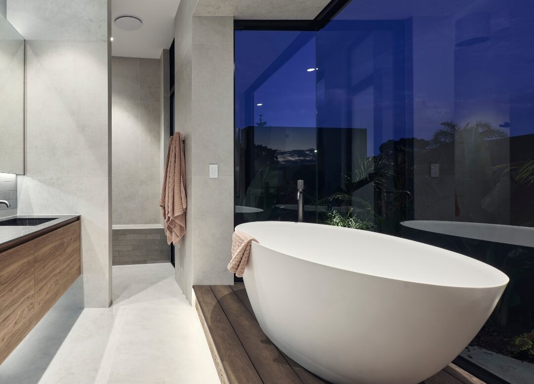 Custom home bathroom featuring a freestanding bath on a raised timber platform, floor-to-ceiling glazing, stone finishes and a floating timber vanity.