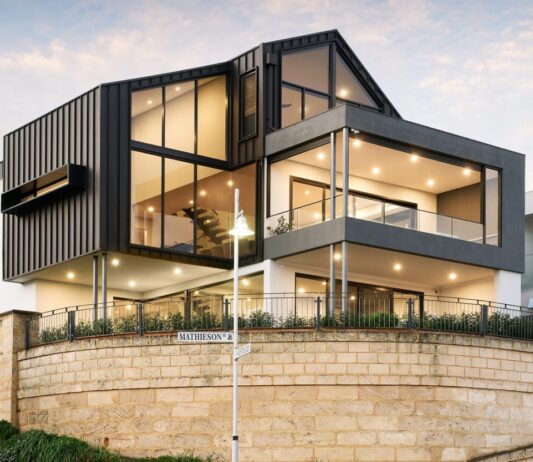 Three-storey custom home on Mathieson Avenue featuring dark vertical cladding, expansive glazing, covered balconies and a limestone retaining wall.
