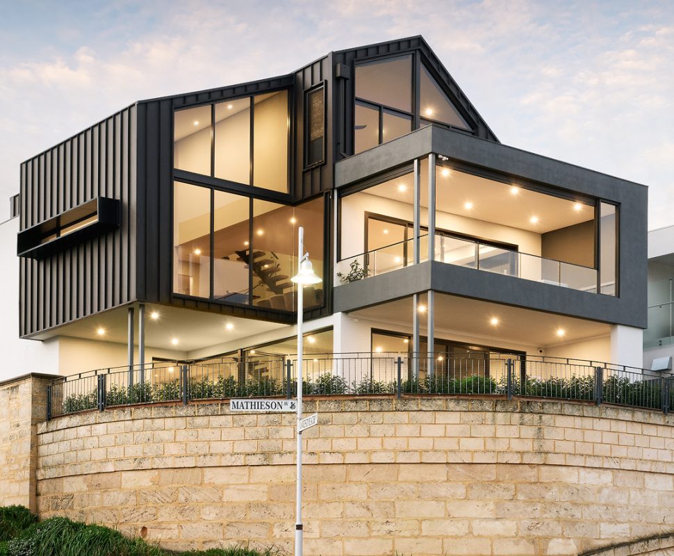 Three-storey custom home on Mathieson Avenue featuring dark vertical cladding, expansive glazing, covered balconies and a limestone retaining wall.