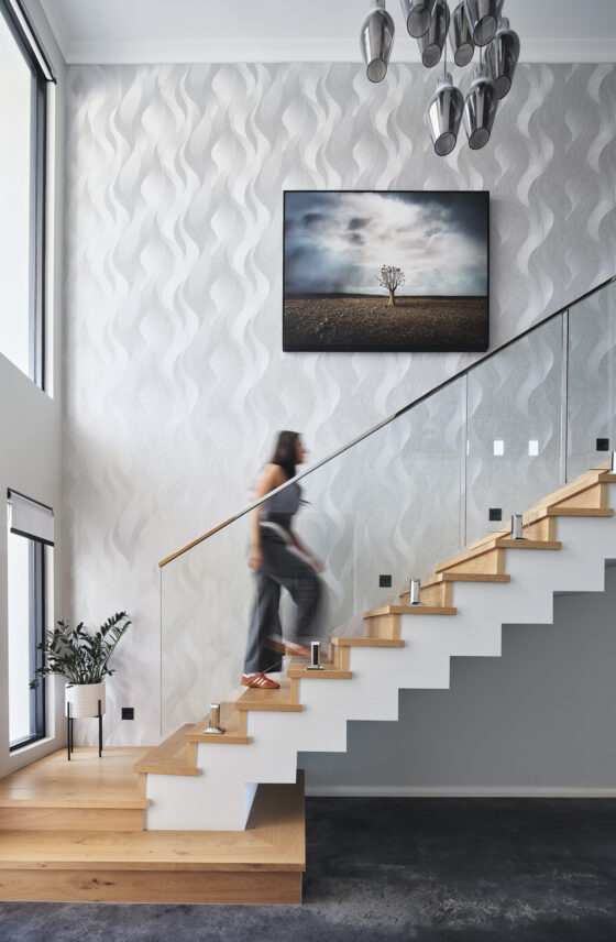 Floating timber staircase with glass balustrading, textured white walls and feature artwork in a custom home.