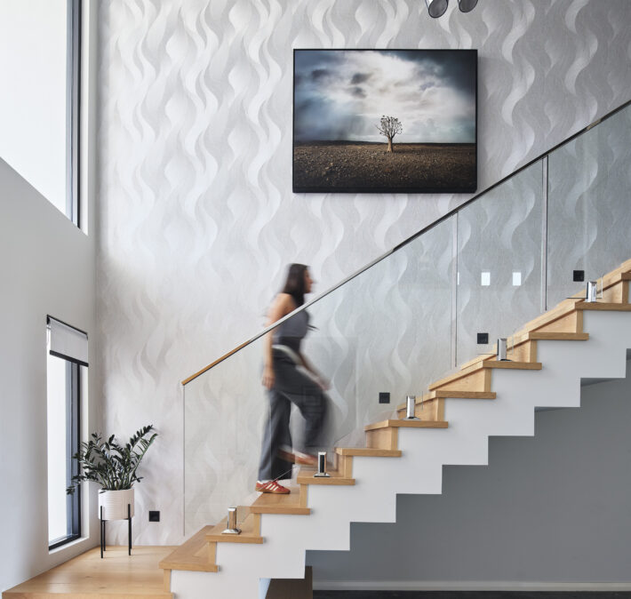 Floating timber staircase with glass balustrading, textured white walls and feature artwork in a custom home.