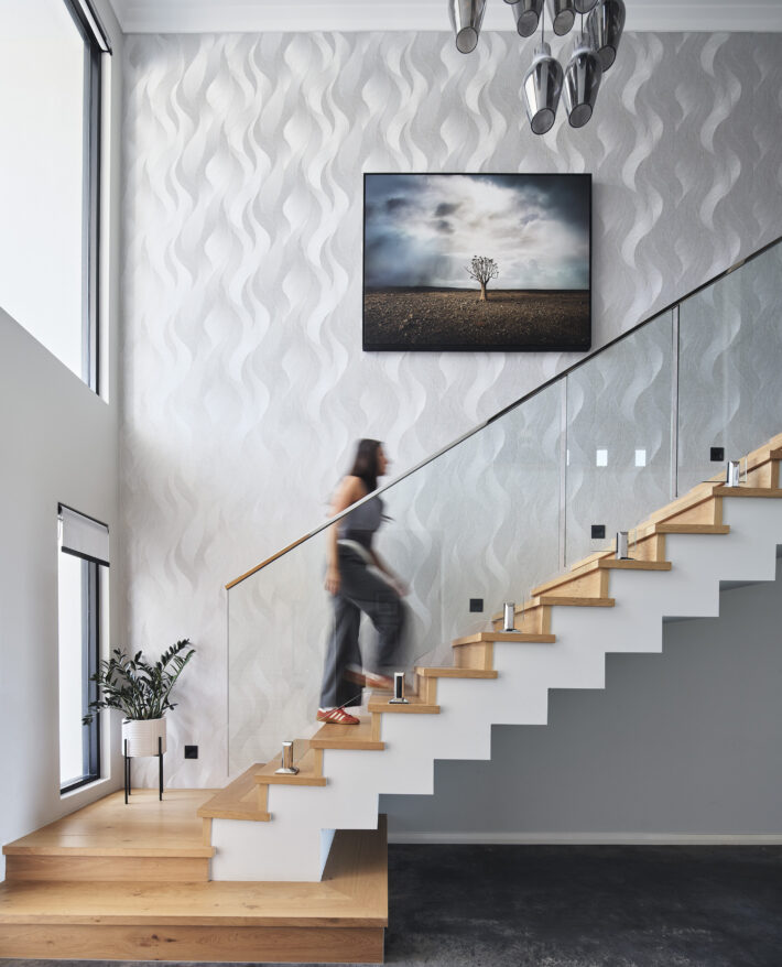 Floating timber staircase with glass balustrading, textured white walls and feature artwork in a custom home.