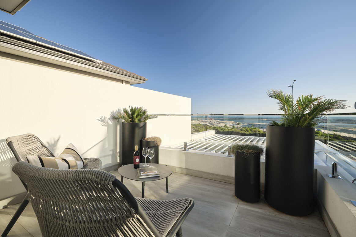 Outdoor balcony with contemporary seating, glass balustrading and expansive coastal views.
