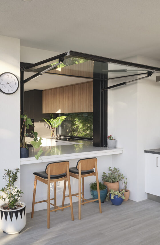 Custom home kitchen featuring a suspended black metal rangehood, timber cabinetry and stone benchtops.