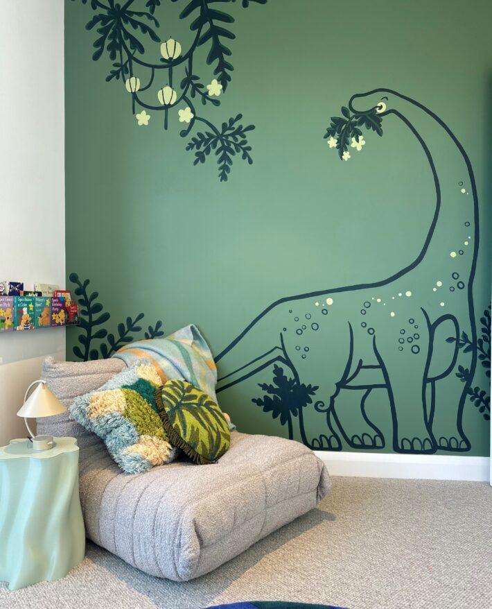 Children's bedroom featuring green illustrated wallpaper, decorative cushions and colourful soft furnishings.