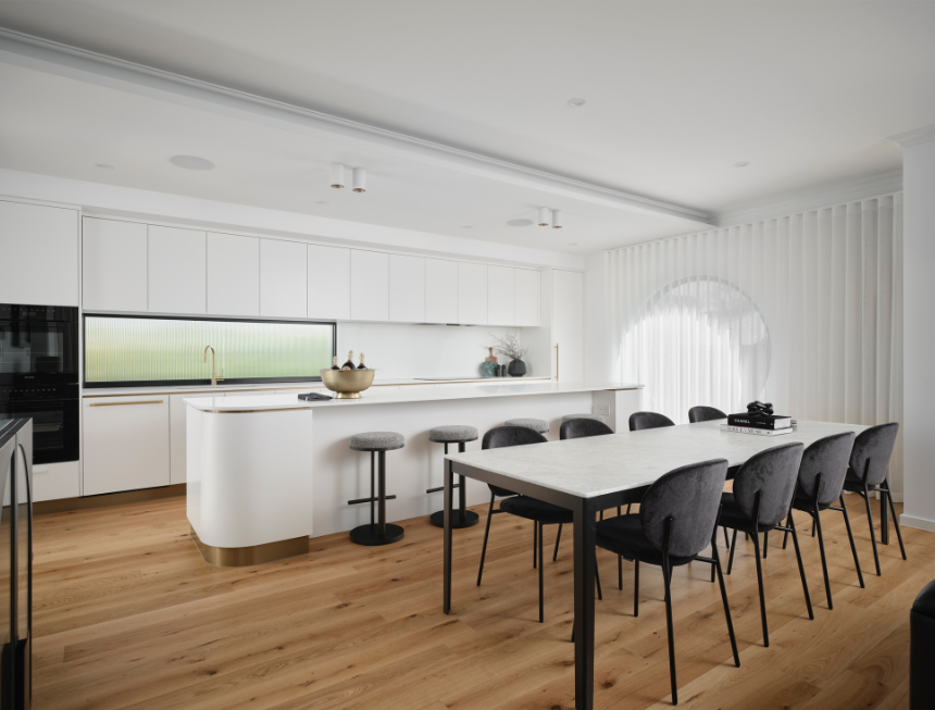 Open-plan kitchen and dining area featuring white cabinetry, stone benchtops and contemporary furniture.