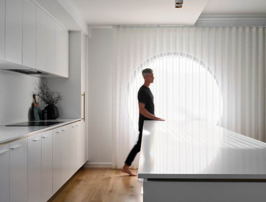 Grosvenor custom home kitchen featuring white cabinetry, stone benchtops and a large circular window with sheer curtains.
