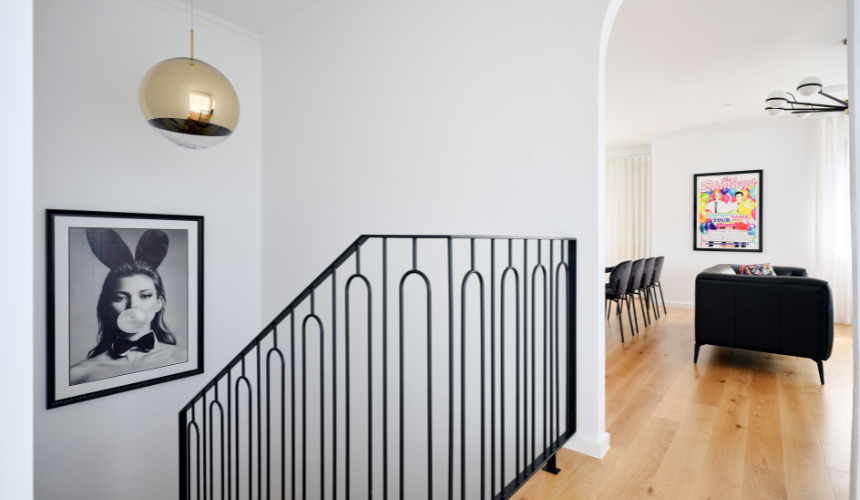 Architectural interior featuring a sculptural pendant light, curved wall detailing and a staircase with dark metal balustrading.