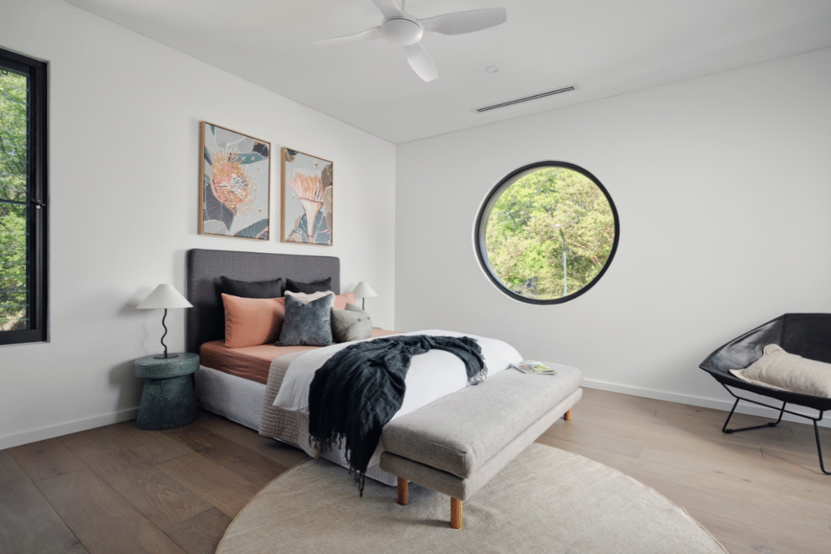 Master bedroom in a Nedlands custom home featuring a circular window, white walls and contemporary furniture.